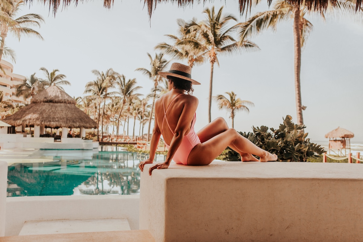 Woman by a resort pool wearing a sunhat.