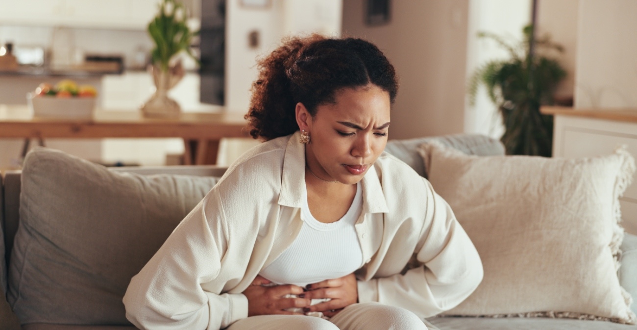A woman sitting on a couch pressing her stomach in pain due to food poisoning symptoms