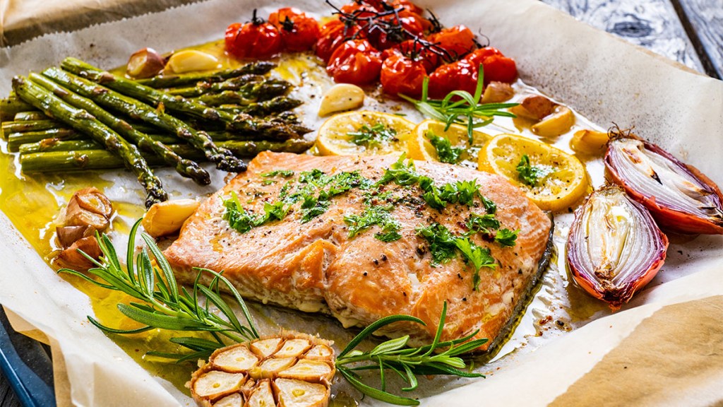 Sheet pan dinner - roasted salmon steak with asparagus, lemon ,rosemary, tomatoes, onion and garlic on cooking pan