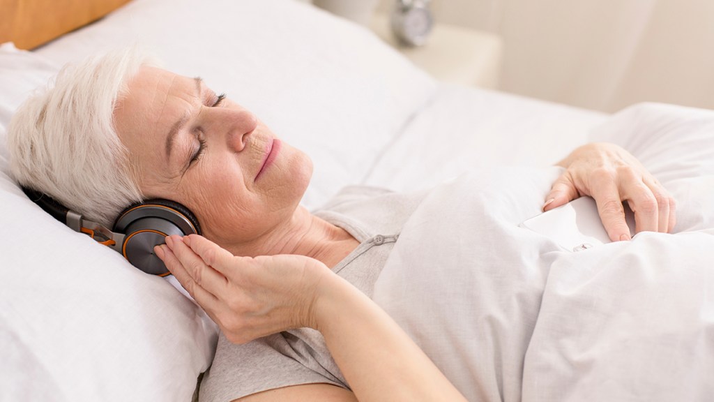 Older woman lying in bed relaxing to music at the 432 hertz frequency