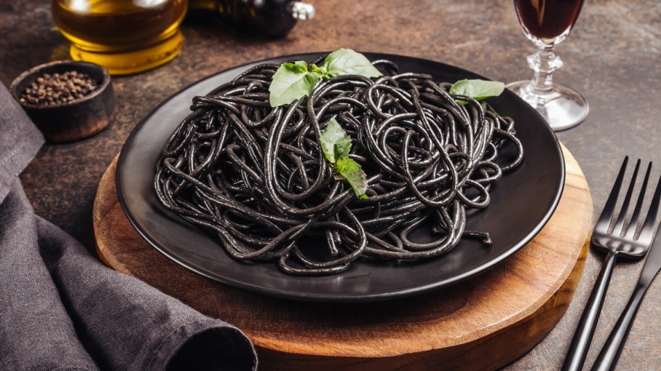 Black pasta - squid ink, with olive oil, basil leaves and parmesan in a black plate on a dark background. Selective focus