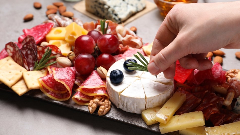 Woman's hands putting rosemary on charcuterie board with various meats and cheeses