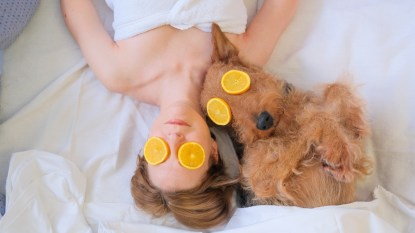 Female and dog laying in bed with Orange face mask having spa day