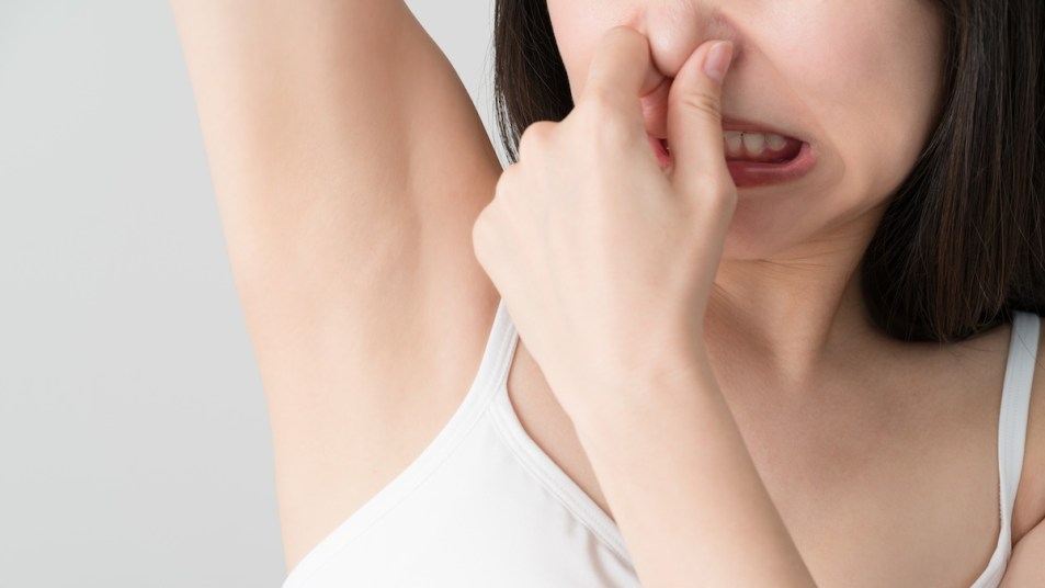 Close-up of woman smelling her armpit and holding her nose