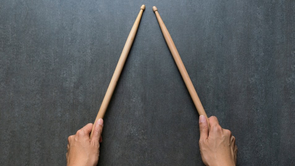 woman holding two drumsticks on gray surface, concept for the rhythm challenge