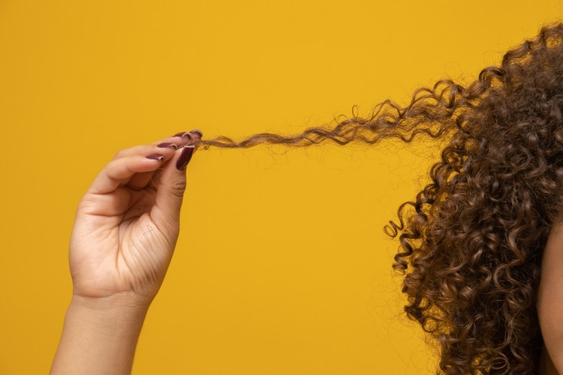 Close-up of a woman pulling on a lock of her curly hair.