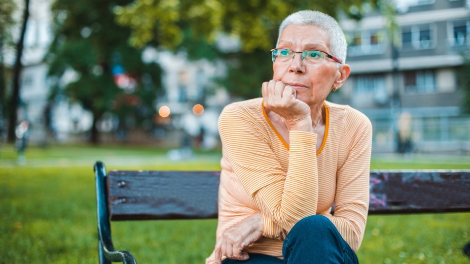 mature woman with glasses sitting on park bench, deep in thought