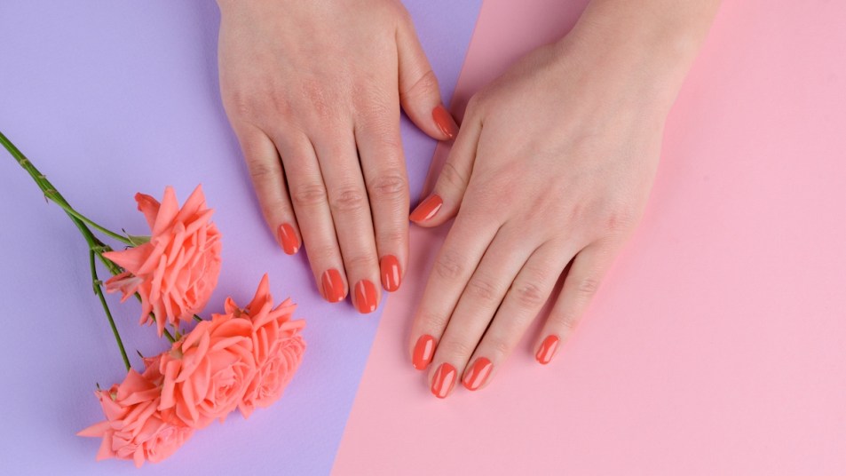 Woman's hands with nails painted coral on pink and purple background with flowers