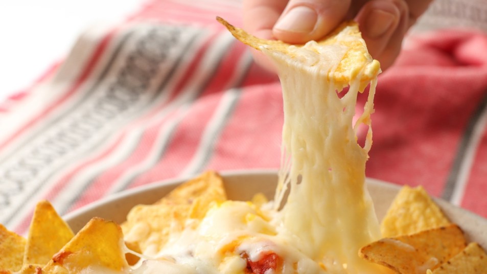 Close-up of woman's hand lifting cheesy nachos