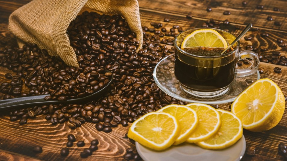 Coffee cup and beans on old kitchen table. Top view with copy space for your text. coffee bag and with sliced ​​lemons on wooden table. Black coffee beans.