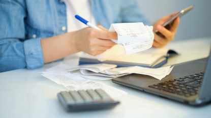 Woman holding pen and receipts, with computer and calculator