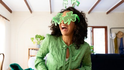 woman dressed in green with shamrock glasses for st patrick's day laughing. Staying at home in self isolation during quarantine lockdown.