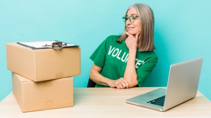 Woman wearing volunteer shirt and sitting at table with laptop, boxes, and clipboard
