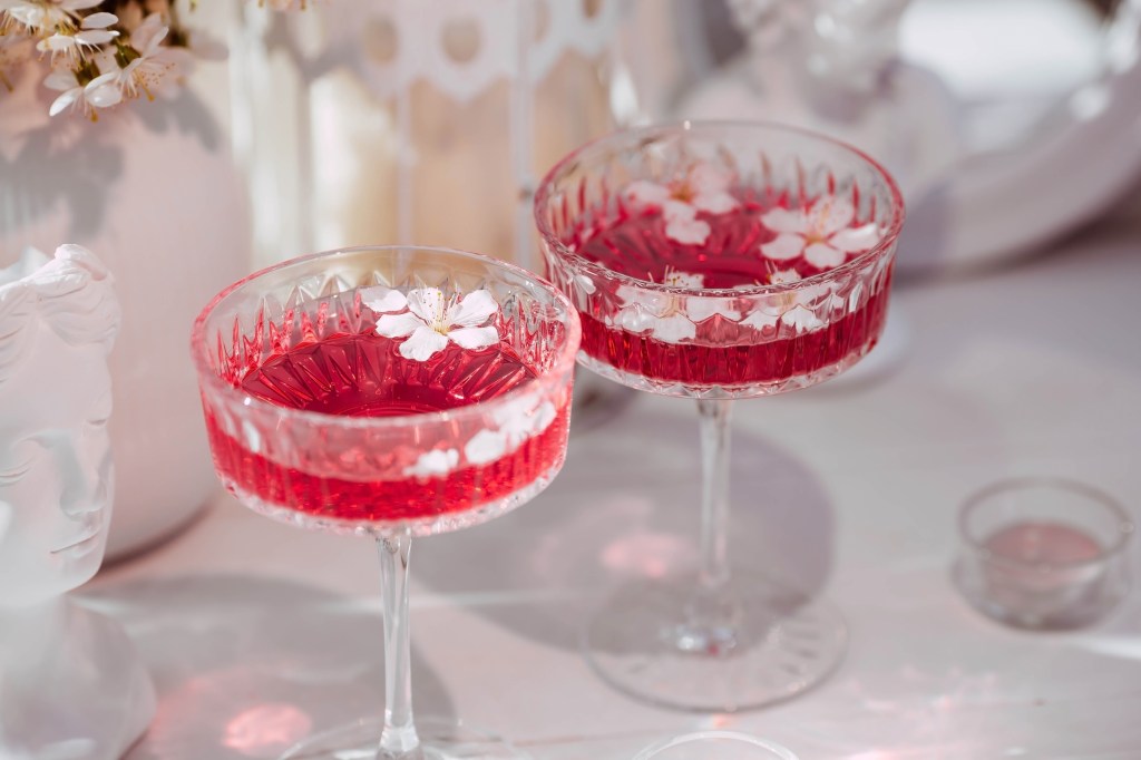 Two fashionable glasses for dessert and champagne with a pink drink and cherry blossoms inside on a light background with hard shadows and highlights. The concept of a party and a holiday.