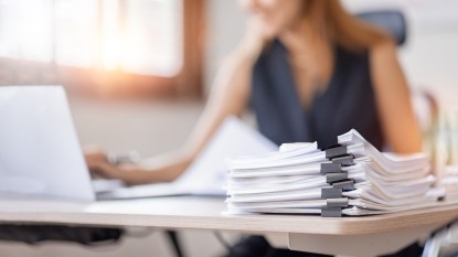 Woman at desk using laptop with stack of tax papers