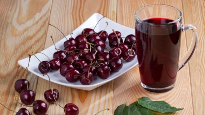 tart cherry juice in glass next to white plate of cherries