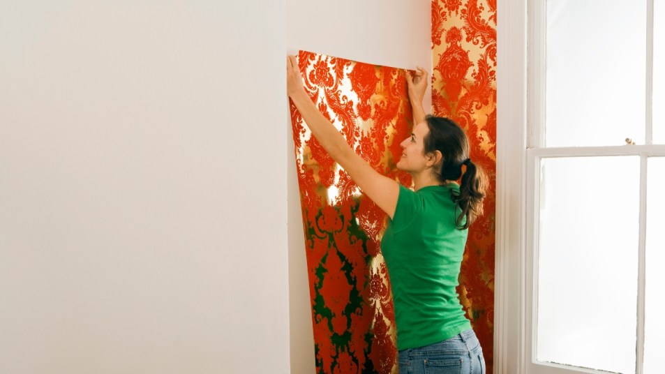 woman hanging red stick on wallpaper to a wall