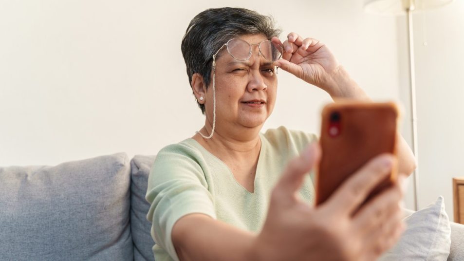 mature woman with glasses, looking at her phone and squinting, vision loss concept