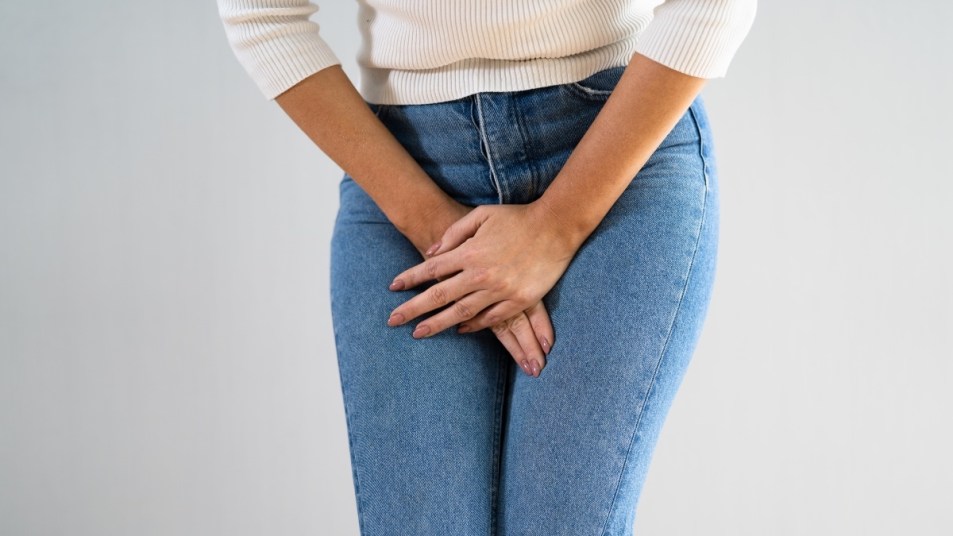 A woman with urinary incontinence holding her hands over her jeans