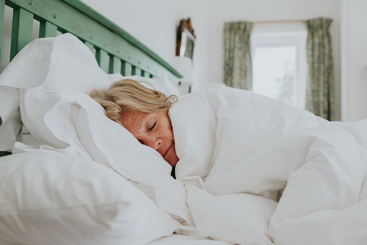 A woman looks so cozy as she is enjoys being wrapped in a thick, white duvet in a double bed.