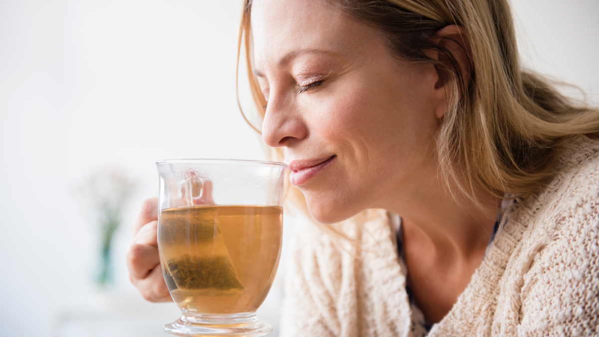 A woman holding a cup of herbal tea to her face while smiling, which is good for a sore throat