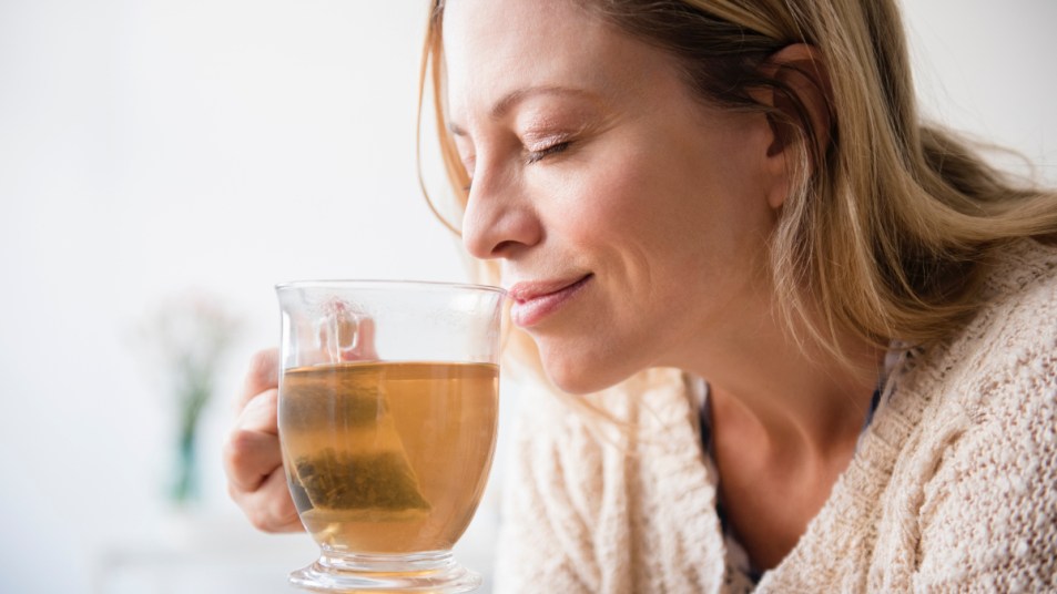 A woman holding a cup of herbal tea to her face while smiling, which is good for a sore throat