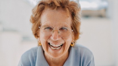 Senior woman with glasses and red hair smiling into camera, full teeth
