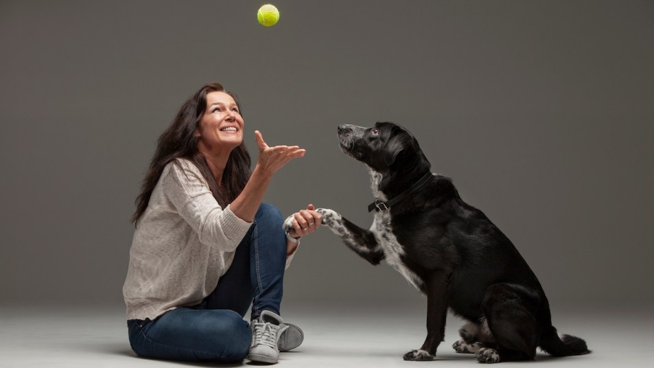 Woman tossing ball to dog while holding its paw