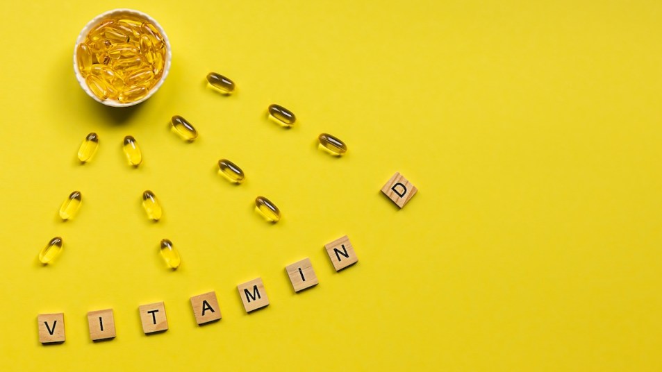 Vitamin D supplements and letters spelling out vitamin D on yellow background