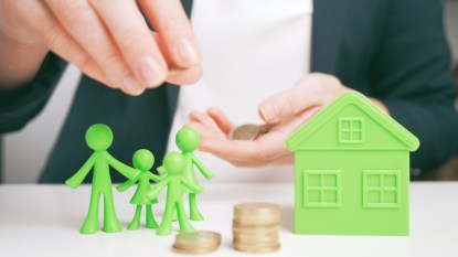 Woman's hands holding coins with green model of family and house