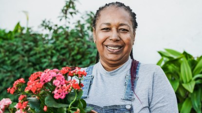 Happy african senior woman smiling on camera while holding flowers at home terrace - Gardening concept