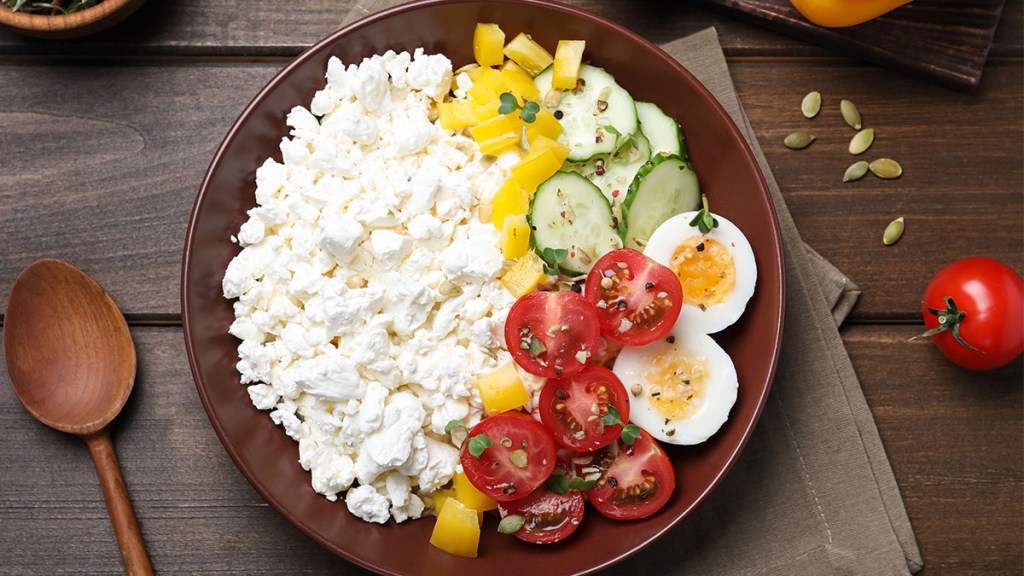 Bowl of keto-friendly cottage cheese with slices of cucumber, egg and tomatoes