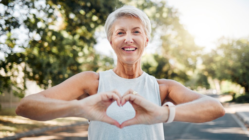 A woman with grey hair wearing a tank top using her hands to make a heart