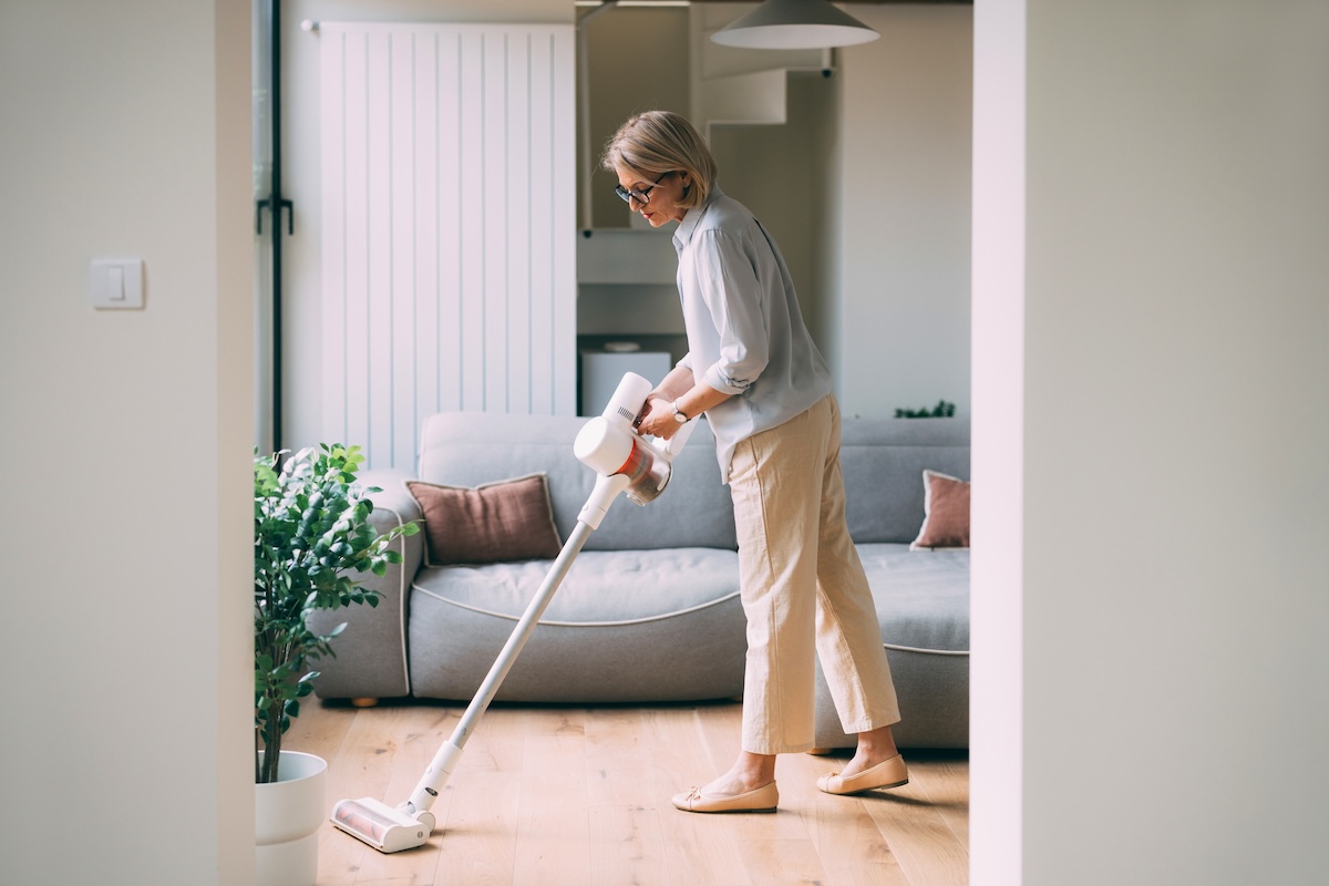 An unidentifiable woman in casual clothing using a cordless vacuum cleaner to tidy up her modern living room.