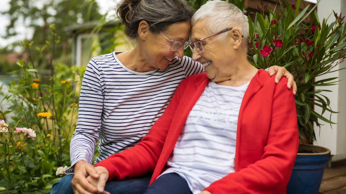 middle-aged woman smiles while holding hands with elderly mother