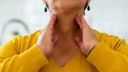 mature woman touching hands to her neck, checking thyroid health