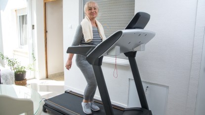 mature woman walking on treadmill doing exercises with towel on neck