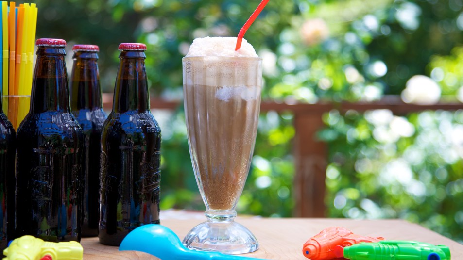 Black Cow drink, also called a root beer float, sitting on a table next to bottles of root beer