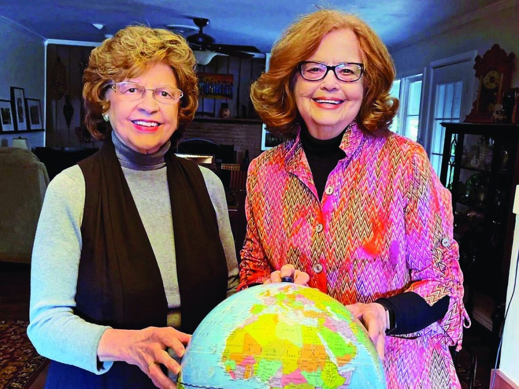 Senior travel buddies Sandy and Ellie together holding globe.