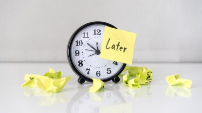 round clock with a black rim on the table, sticky note stuck to it that says "later", crumpled notes nearby, to signify procrastination