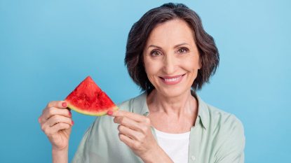 senior woman smiling and holding up a slice of watermelon near her face