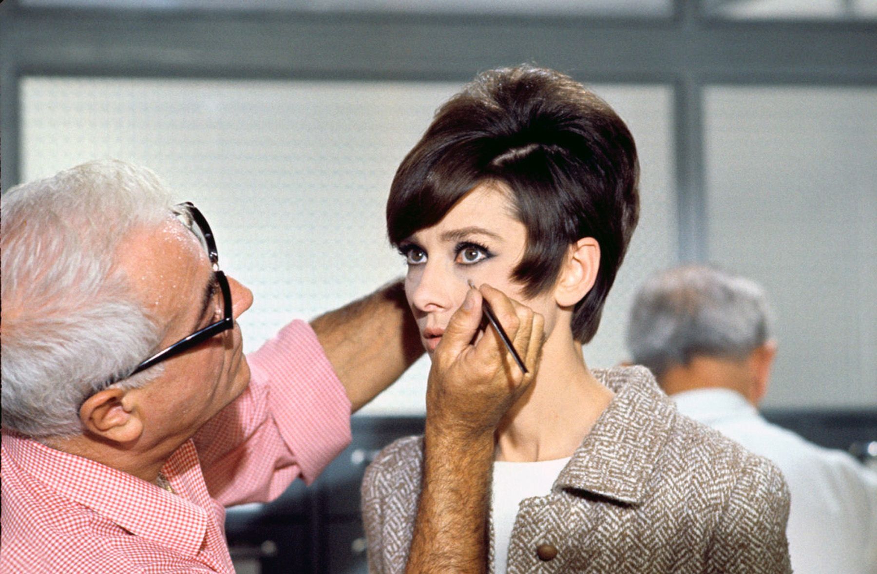 Audrey Hepburn having her eye makeup done by a makeup artist