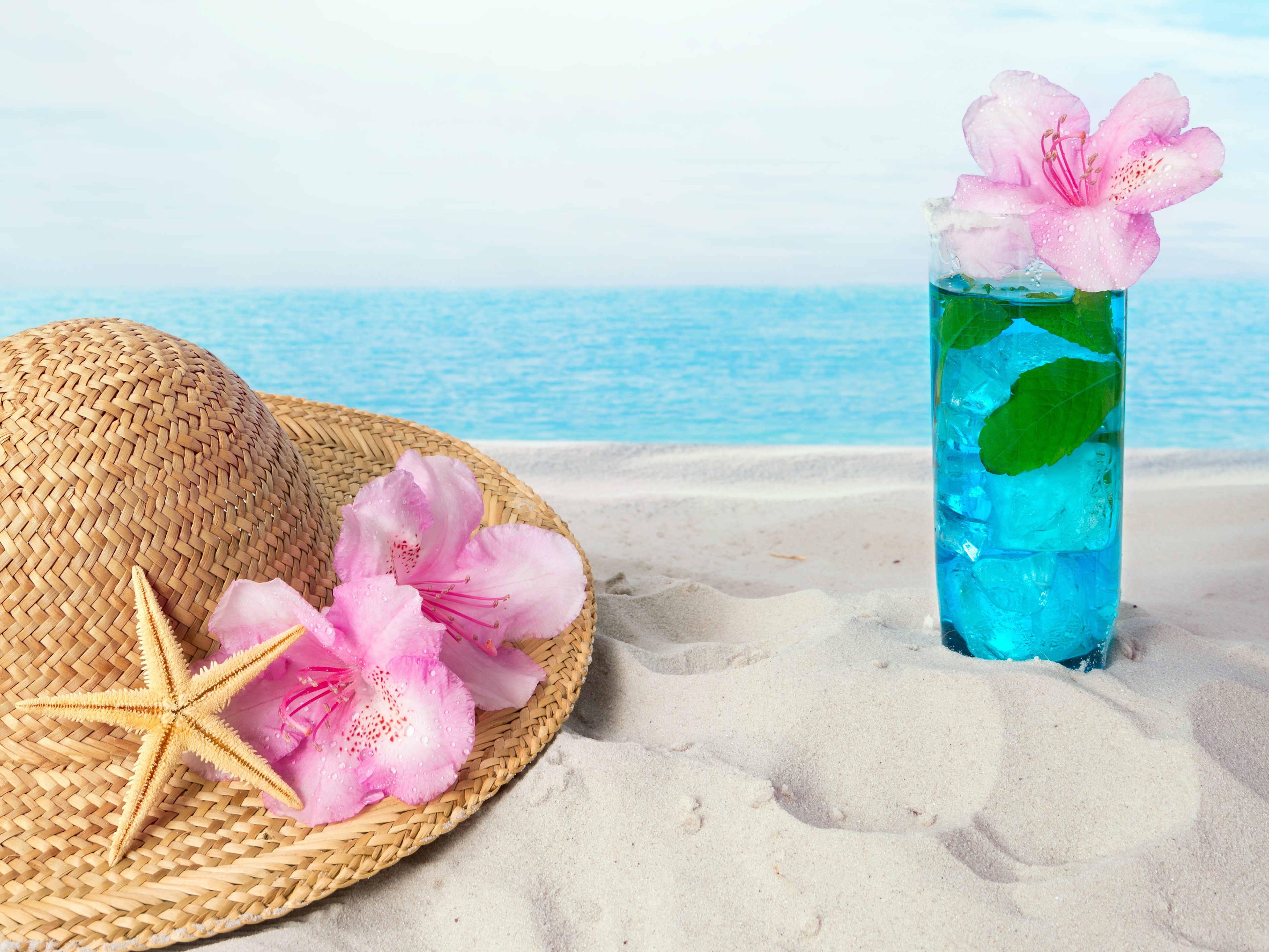 Blue drink on the beach alongside a sunhat and sea shells