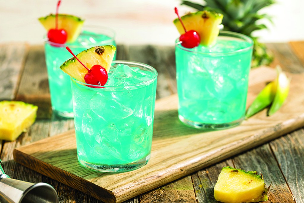 Three tropical blue-hued cocktails garnished with cherries and pineapple slices