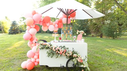 Photo of an ice cream party stand with pink balloons, white umbrella and ice cream cones