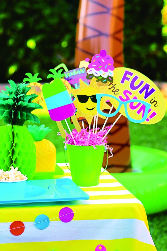 Bucket filled with photo booth props like suns and sunglasses and signs that say "Fun in the Sun"