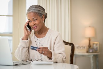 Older woman paying for something over the phone with a credit card and smiling