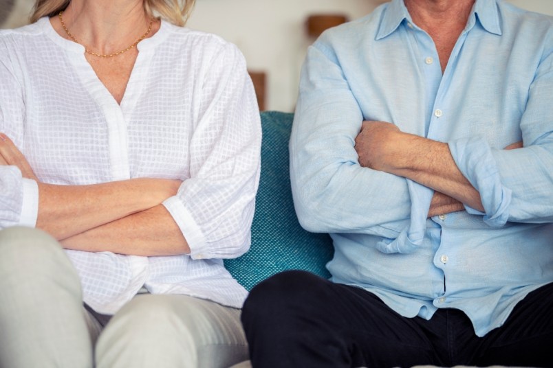 Mature couple fighting at home sitting on the sofa. They are both looking angry and have their arms crossed