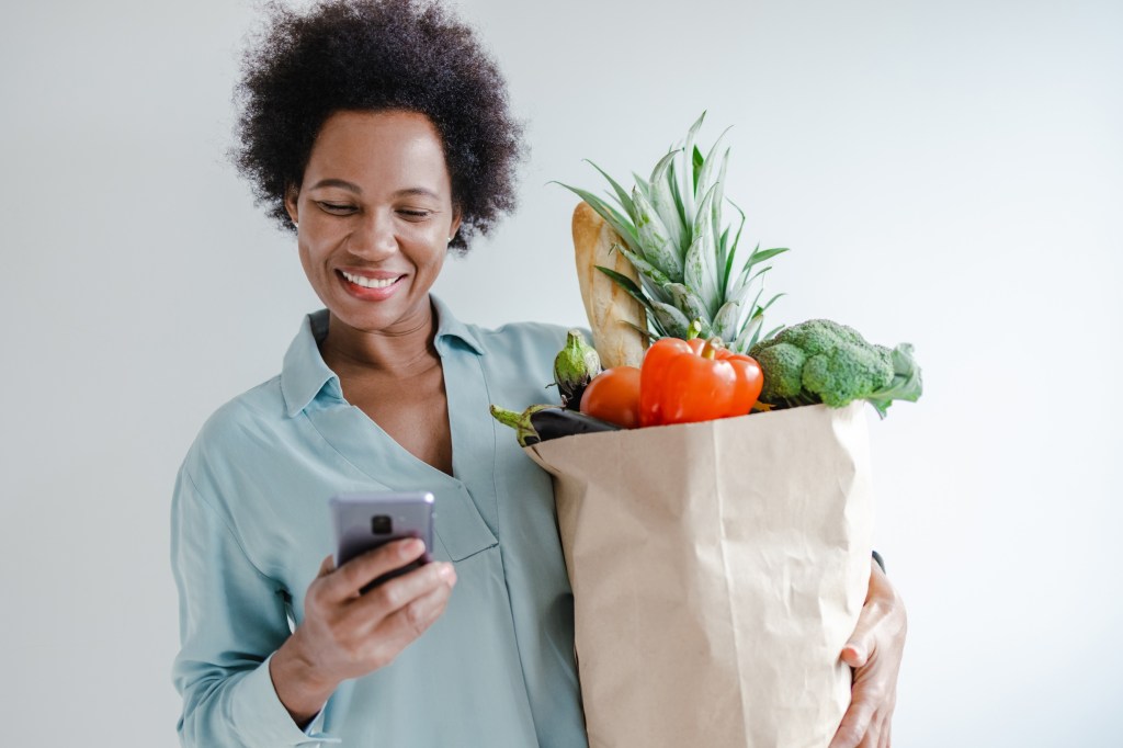 woman holds bag full of groceries at home (driving apps to make money)