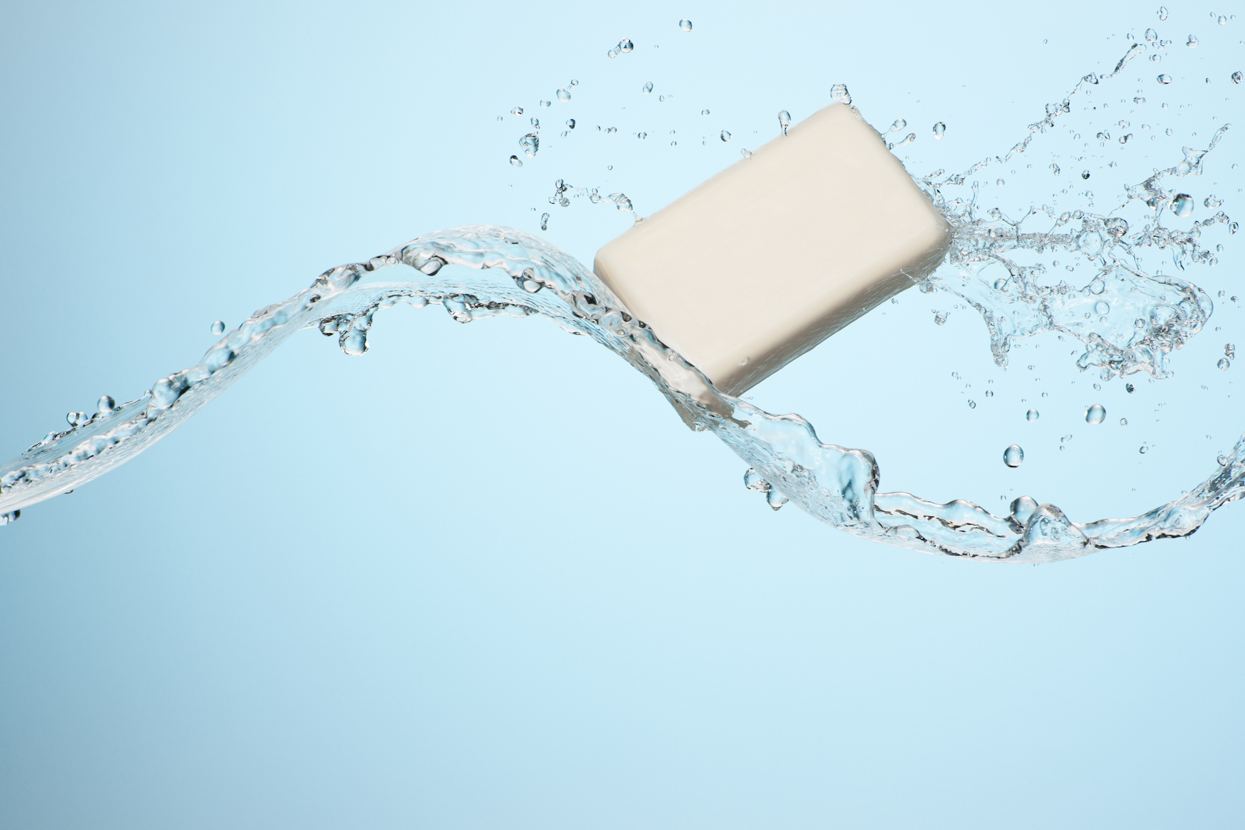 Big flowing splash of clean refreshing water with a white bar of soap in studio on a light blue background 